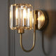 A close up of the brushed brass and crystal wall light on a grey wall.
